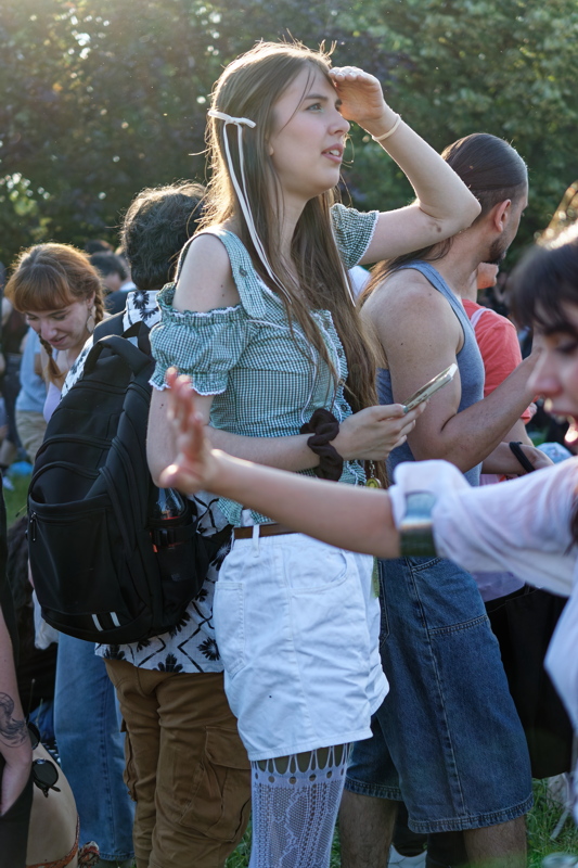 6 - Person with long hair wearing a green checkered top and a white skirt at an outdoor gathering
